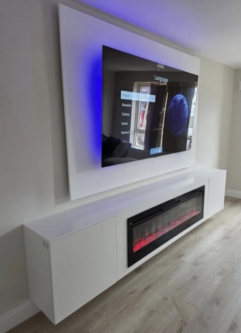 Angled view of white floating media wall with recessed 77-inch OLED TV and built-in electric fireplace with flame effect