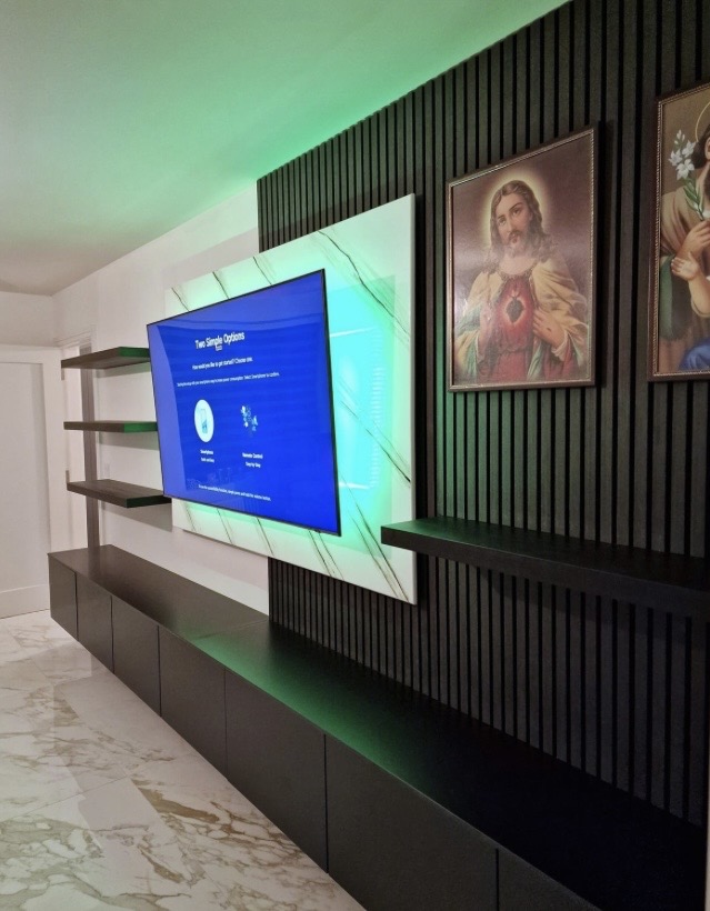 Angled view of charcoal acoustic feature wall with green LED TV backlight, floating shelves and black matte cabinet on marble floor
