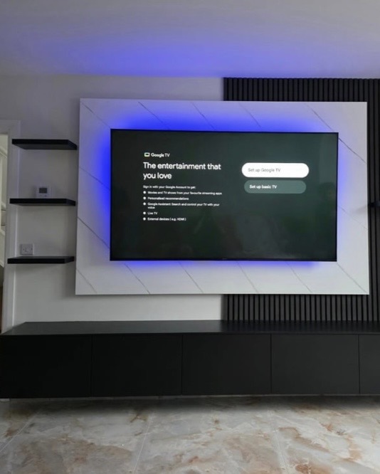 White media wall with 77-inch OLED TV, blue LED backlight, charcoal acoustic slat panel side wall and black floating cabinet with shelves