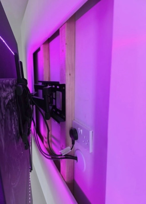Behind-the-TV detail showing concealed cabling, full-motion double-arm bracket, double socket and RGB LED backlight