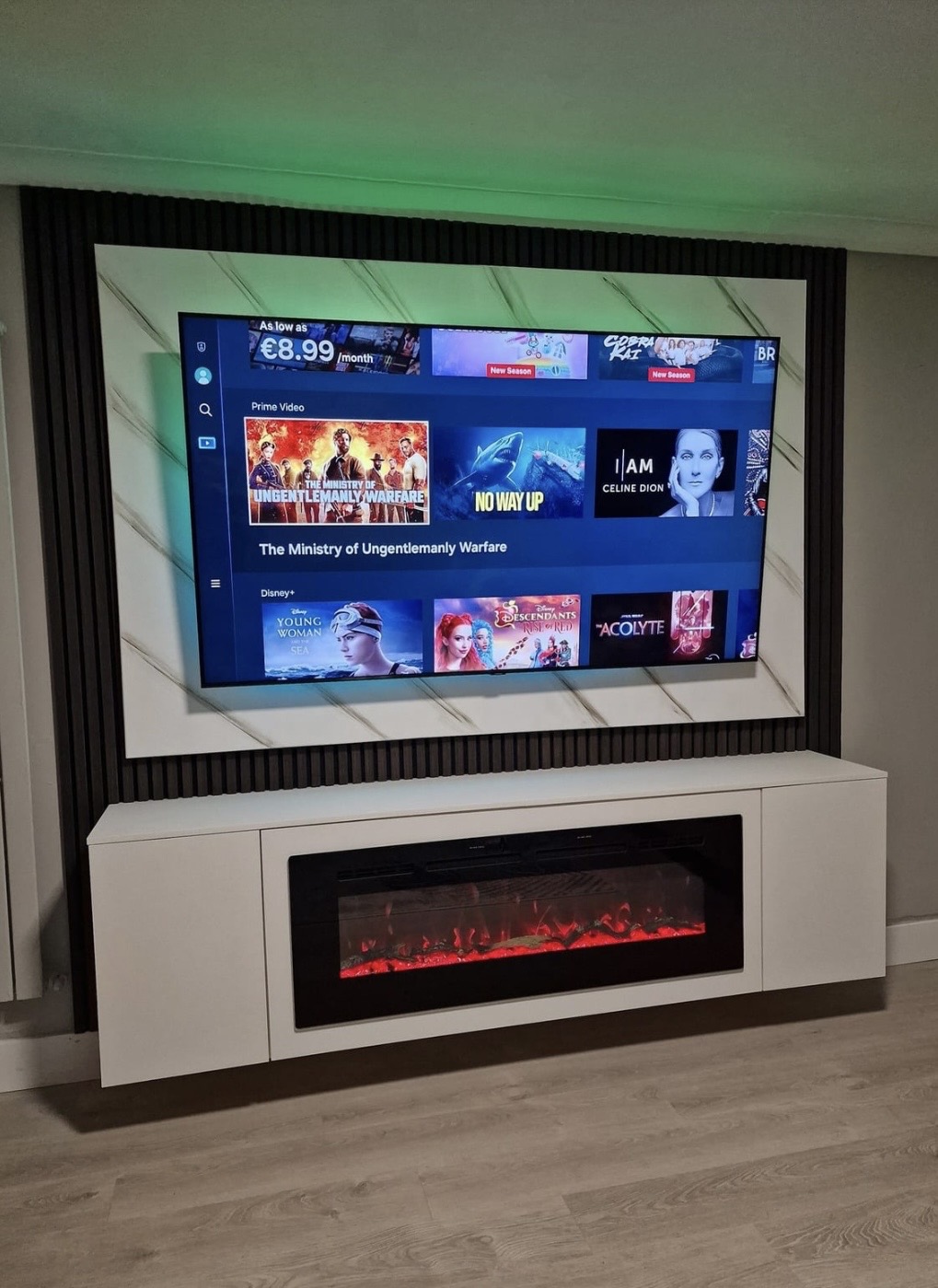 Front view of media wall with marble TV back panel, green LED backlight and 220 cm white floating unit with 50-inch electric fireplace