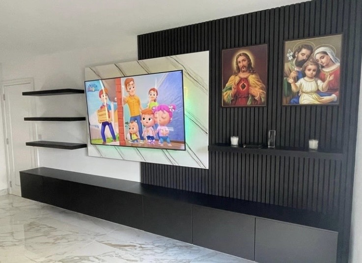 Front view of media wall with 65-inch TV showing children's programme, charcoal slat panels and floating black shelves